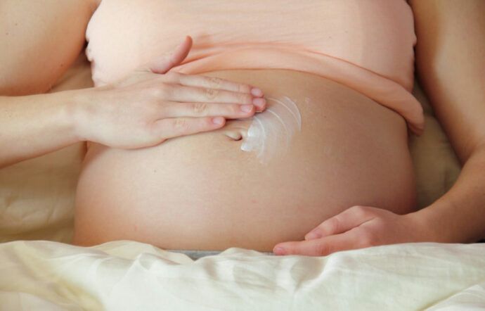 schwangere frau cremt bauch ein