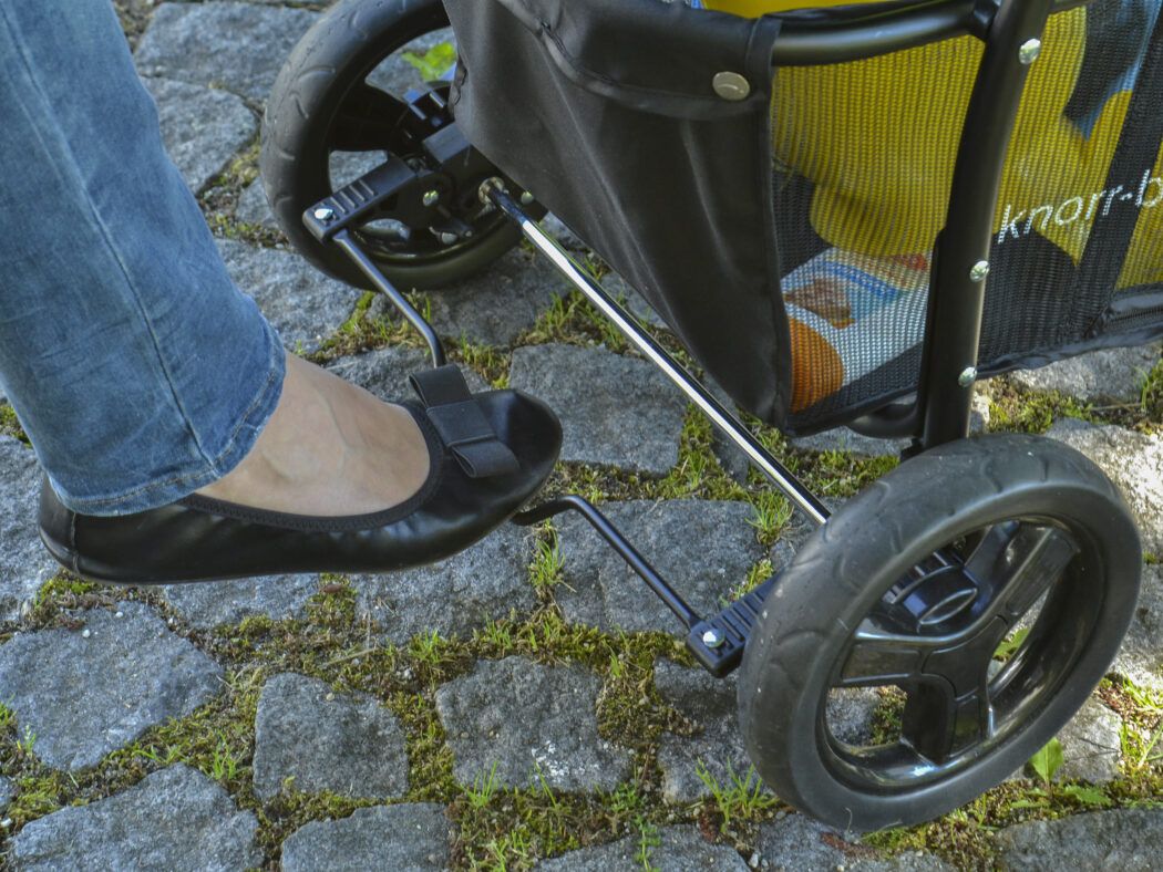 Mit dem Fuß bedienst Du die Feststellbremse, leider ist diese nicht besonders schuhschonend.