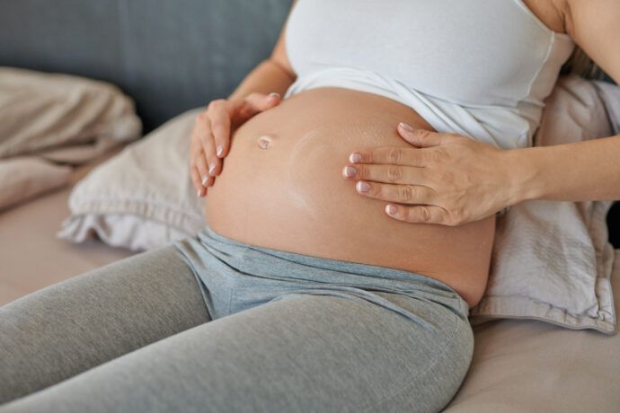 frau cremt ihren schwangerschaftsbauch ein