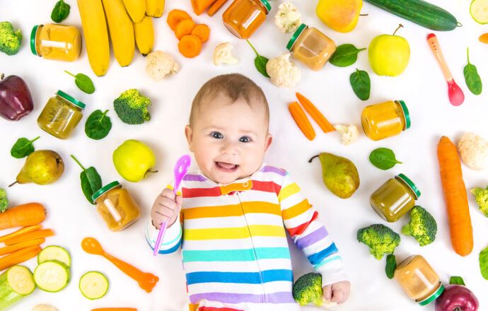 beikostplan baby hält löffel liegt neben obst gemüse gläschen