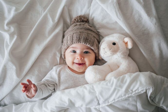 heilwolle baby anwendung bei wundem po lachender säugling liegt im bett mit kuscheltier schaf