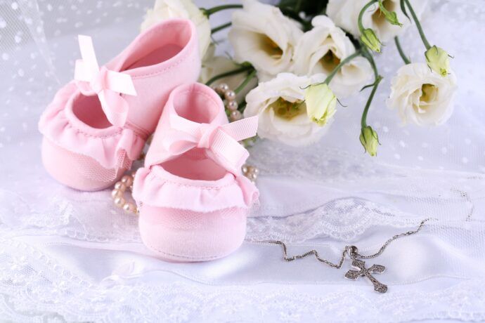 fürbitten taufe blumen kreuz perlen und rosa baby schuhe liegen auf weißem taufkleid