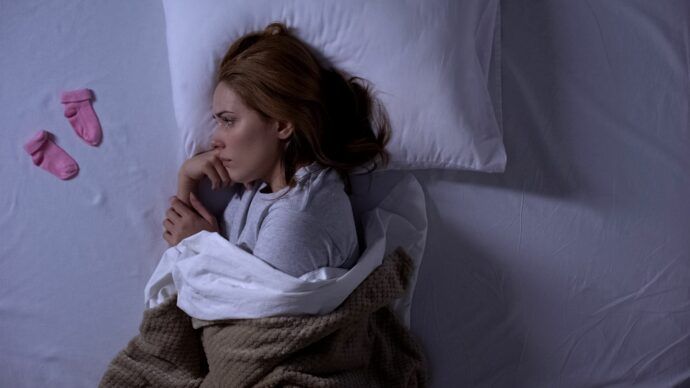 missed abortion welche ssw, blutung, ausschabung, wahrscheinlichkeit, fehldiagnose verhaltene fehlgeburt, traurige frau im bett mit babysocken