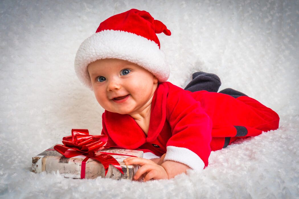 nikolaus geschenk baby liegt froehlich im santa kostuem auf decke