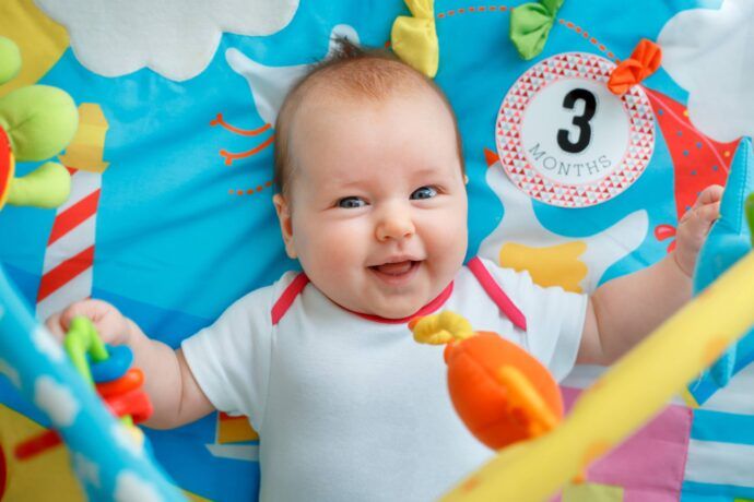 fröhliches baby 3 monate liegt und greift babyspielzeug auf bunter spieldecke