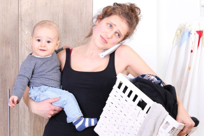 frau mit baby auf dem arm telefoniert und trägt wäschekorb, anfängerfehler baby, erstes kind