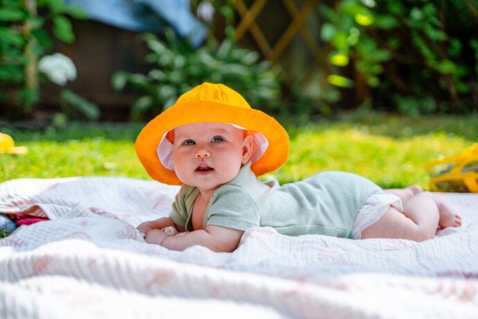 baby bei hitze tipps, hitzwelle mit baby, sommerbaby, baby mit sonnenhut liegt auf einer decke im garten