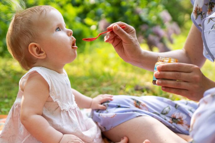 babybrei unterwegs erwärmen, brei unterwegs aufwärmen, brei im urlaub warm machen. babygläschen kalt geben, frau füttert baby mit brei draußen