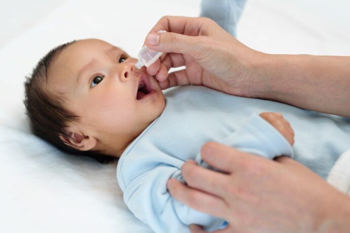 nasentropfen baby liegt auf rücken und bekommt kochsalzlösung in die nase getropft