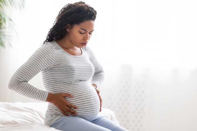 Schwangere Frau fasst sich an den Bauch, harter Bauch in der Schwangerschaft 1. Trimester, 2. Trimester, 3. Trimester