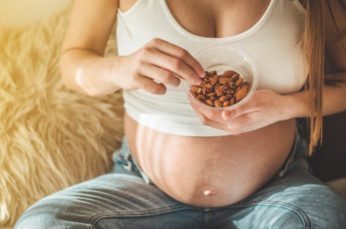 nuesse schwangerschaft, schwangere frau mit babybauch isst frische nuesse, mandeln walnuesse, gesunde ernaehrung in der schwangerschaft