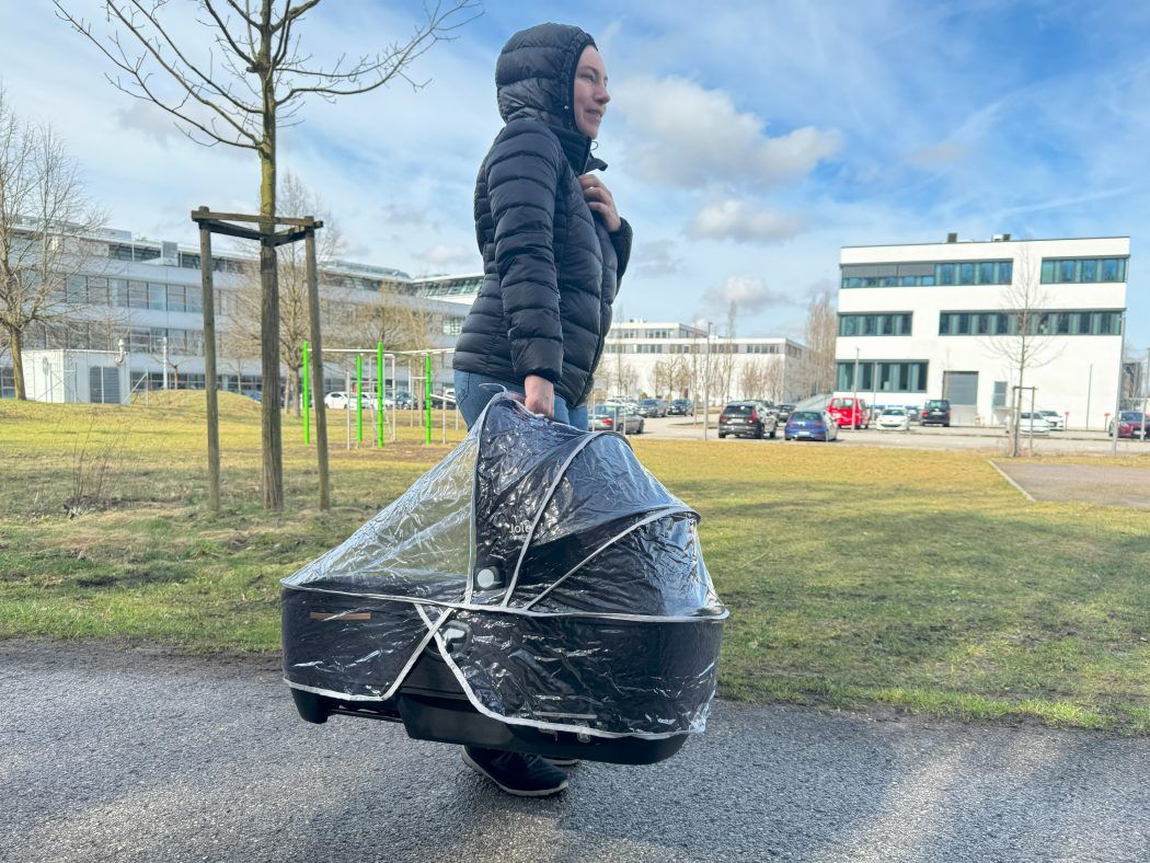 joie calmi r129 test person trägt babywanne mit regenverdeck