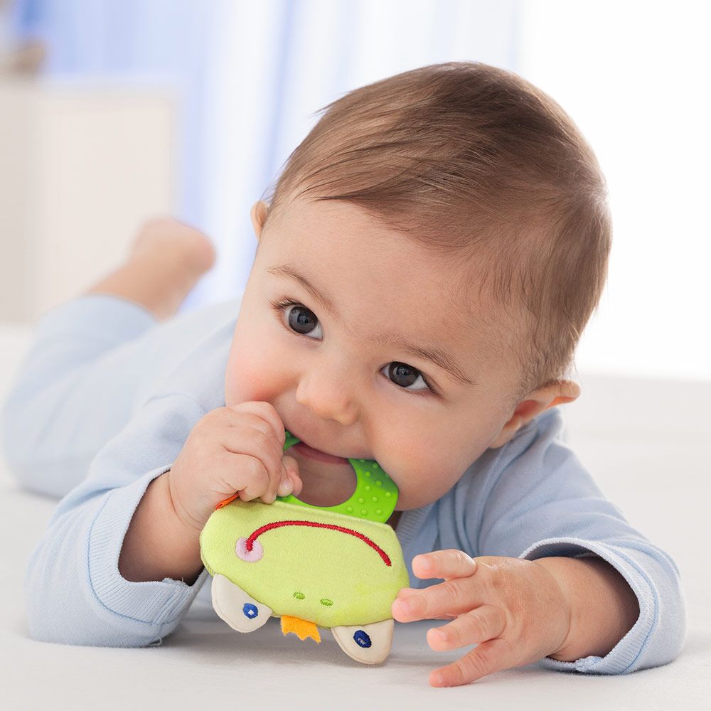 greifen lernen, baby in bauchlage haelt greifling im affengriff mit ganzer hand fest beisst in das babyspielzeug