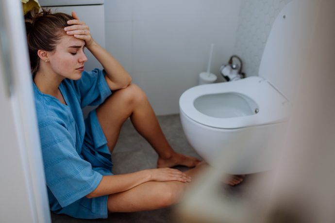 übelkeit schwangerschaft, schwangere frau mit morgenübelkeit sitzt im badezimmer auf dem boden vor der toilette