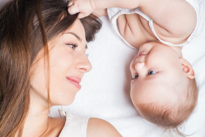 haarausfall nach schwangerschaft symbolbild niedliches baby zieht laechelnder mutter im liegen sanft an haaren