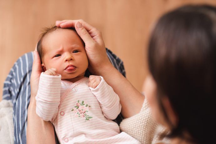 baby streckt zunge raus neugeborenes liegt bei mutter auf schoss