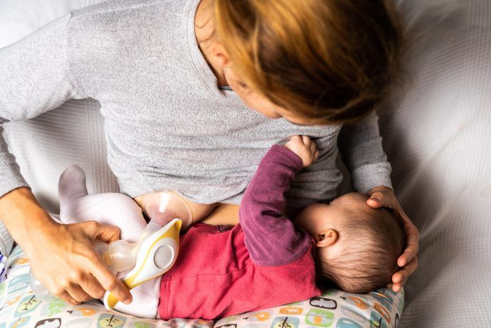 Mutter stillt Baby und pumpt gleichzeitig Milch mit Milchpumpe ab, Stillen und Abpumpen kombinieren ohne Saugverwirrung