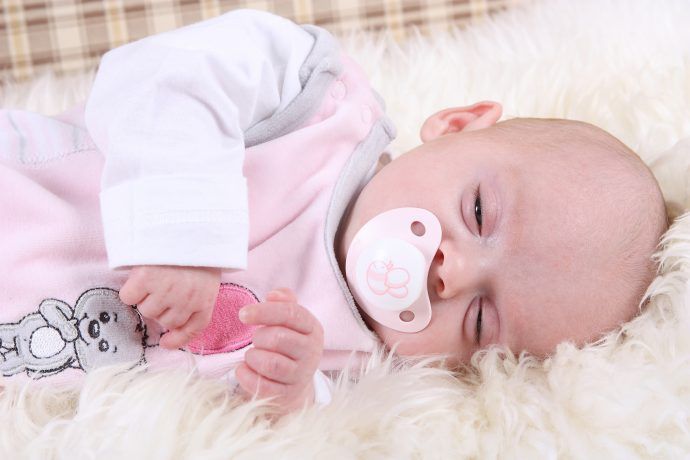 baby schlaeft mit offenen augen und schnuller auf lammfell