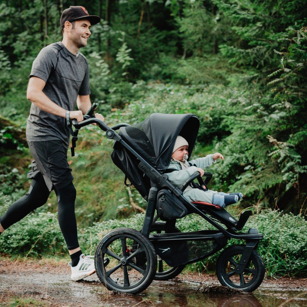 kinderwagen zum joggen vater läuft mit jogger mit sitzendem baby durch wald