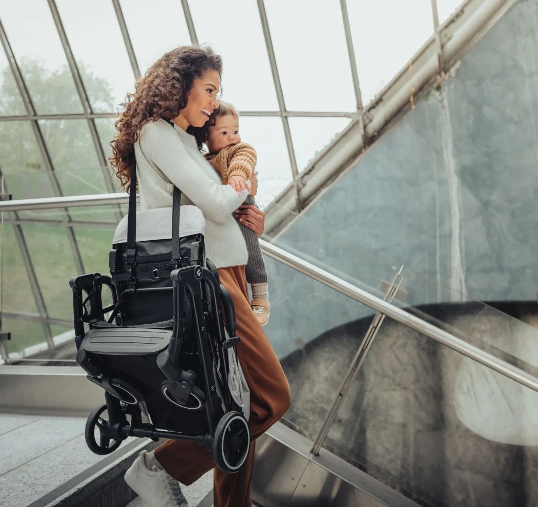 mutter trägt hauck reisebuggy travel n care plus mit tragegurt hält baby im arm